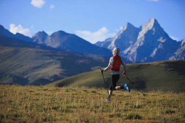 Fitness kadın patika koşucusu arka planda karlı dağlarla çayırlarda koşuyor.