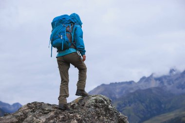 Sırt çantalı bir kadın yüksek irtifada dağ tepesinde yürüyüş yapıyor. Uzakta bir göl var.
