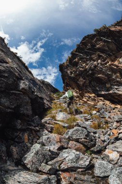 Sırt çantalı bir kadın yüksek rakımlı dağlarda dik yamaçlara tırmanıyor.