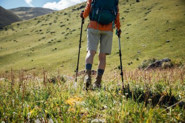Sırt çantalı bir kadın yüksek irtifada dağ tepesinde yürüyüş yapıyor. Uzakta bir göl var.