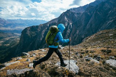 Sırt çantalı bir kadın yüksek rakımlı dağlarda dik yamaçlara tırmanıyor.