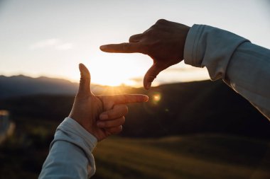Gün batımına karşı resim çerçevesi şeklinde eller