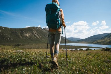 Sırt çantalı bir kadın yüksek irtifada dağ tepesinde yürüyüş yapıyor. Uzakta bir göl var.