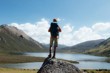Sırt çantalı bir kadın yüksek irtifada dağ tepesinde yürüyüş yapıyor. Uzakta bir göl var.