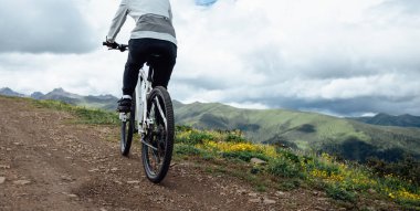 Çiçekli çayır dağ yolunda insanlar dağ bisikleti sürüyor.