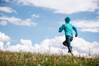 Fitness kadın koşucusu çiçek açan çayırların tepesinde koşuyor.