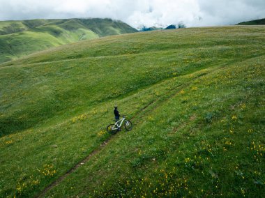 Çiçekli çayır dağ patikasında dağ bisikleti süren kadının hava manzarası.
