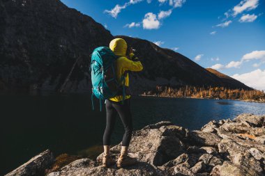 Sırt çantalı bir kadın, sonbahar yüksek irtifada dijital bir kamerayla fotoğraf çekiyor.