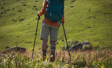 Sırt çantalı bir kadın yüksek rakımlı çayırlarda yürüyüş yapıyor. 