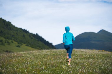 Fitness woman runner running at flowering grassland mountain top clipart