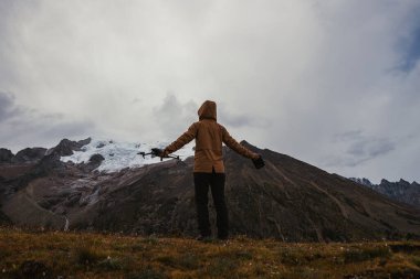 Fotoğrafçı, yüksek rakımlı çayırların tepesindeki bir dron ile karlı dağın fotoğrafını çekiyor.