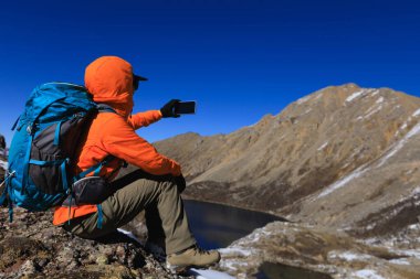Sırt çantalı bir kadın yüksek irtifada telefonuyla fotoğraf çekiyor.