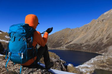 Sırt çantalı kadın fotoğrafçı yüksek irtifada dağın tepesinde oturuyor. 
