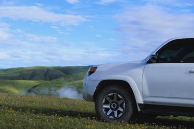 Offroad vagonu mavi gökyüzünün altında çiçek açan çayır dağında