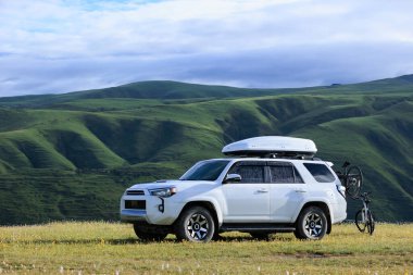 Offroad arabası mavi gökyüzünün altında çiçek açan çayır dağında bisiklet taşıyor.