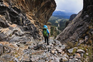 Sırt çantalı bir kadın yüksek rakımlı dağlarda dik yamaçlara tırmanıyor.