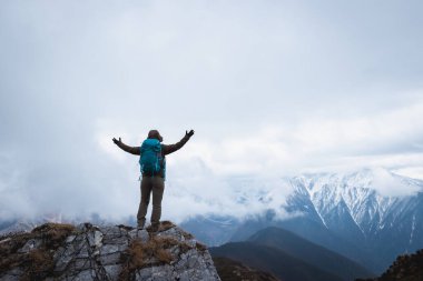 Sırt çantalı kadın yürüyüşçü, Tibet 'teki kar kaplı dağlara bakan dağın tepesindeki manzaranın tadını çıkar.