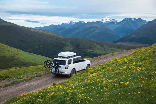 Внедорожник с велосипедами на цветущей травянистой горе под голубым небом