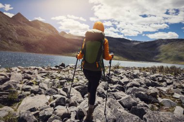 Yükseklerdeki dağlarda yürüyüş yapan bir kadın, güzel bir göle doğru yürüyor.