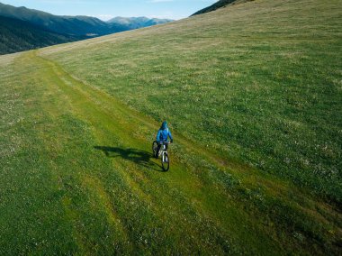 Çiçekli çayır dağ patikasında dağ bisikleti süren kadının hava manzarası.