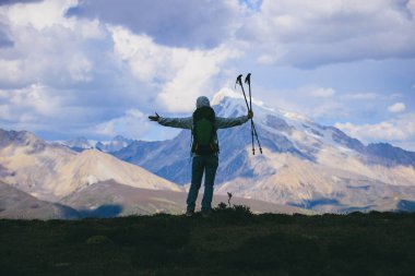 Sırt çantalı kadın kollarını kar kaplı dağa aç günbatımında yüksek irtifa dağının tepesinde.