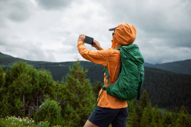 Yürüyüş yapan kadın yüksek irtifa orman tepesinde fotoğraf çekmek için akıllı telefon kullanıyor.