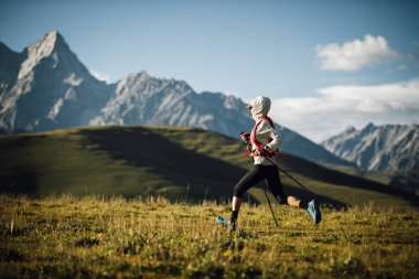 Fitness kadın patika koşucusu arka planda karlı dağlarla çayırlarda koşuyor.