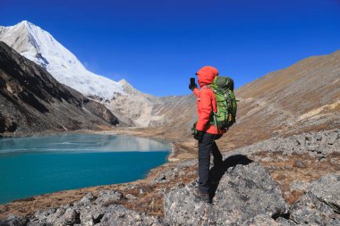 Sırt çantalı bir kadın yüksek irtifada akıllı telefonuyla fotoğraf çekiyor.