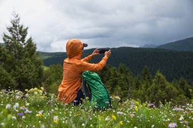 Yürüyüş yapan kadın yüksek irtifa orman tepesinde fotoğraf çekmek için akıllı telefon kullanıyor.