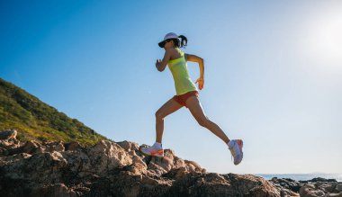 Güneş doğarken deniz kenarındaki kayalarda koşan atletik kadın