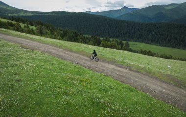 Çiçekli çayır dağ yolunda dağ bisikleti süren kadının hava manzarası.