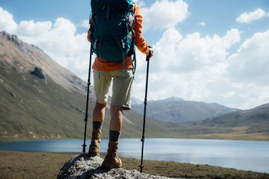 Deri botlar giymiş yürüyüş yapan yürüyüş yapan bacaklar yüksek dağın tepesinde, uzakta bir göl var.