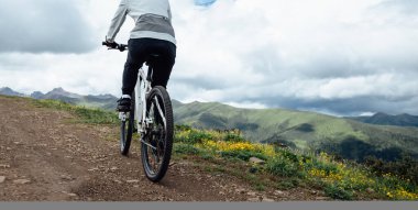 Çiçekli çayır dağ yolunda insanlar dağ bisikleti sürüyor.