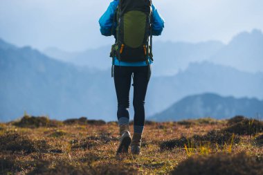 Sırt çantalı bir kadın günbatımında yürüyüş yapıyor yüksek irtifa dağının tepesinde