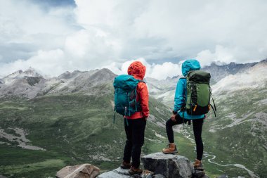 Bulutlu gökyüzünün altındaki dağlık araziye hayran yürüyüşçüler