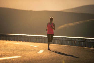 Gün batımında dağ yolunda koşan kadın koşucu