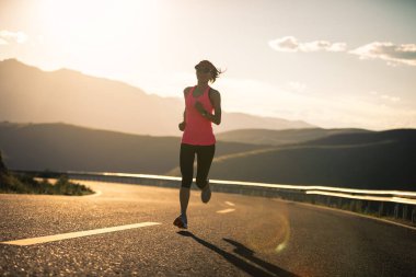 Gün batımında dağ yolunda koşan kadın koşucu