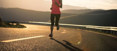 Gün batımında dağ yolunda koşan kadın koşucu
