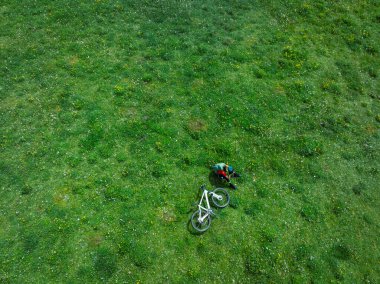 Çiçekli çayır dağ patikasında dağ bisikleti süren kadının hava manzarası.