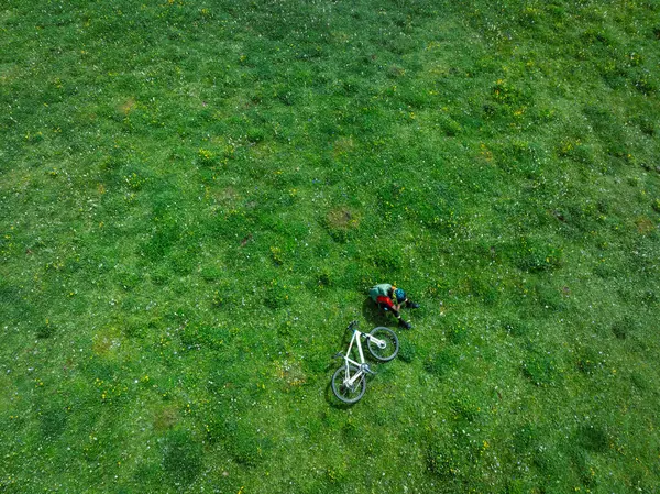 Çiçekli çayır dağ patikasında dağ bisikleti süren kadının hava manzarası.