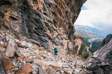 Sırt çantalı bir kadın yüksek rakımlı dağlarda dik yamaçlara tırmanıyor.