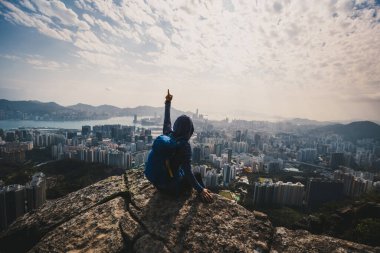 Uçurumun kenarında oturan kadın Hong Kong 'un güzel manzarasının tadını çıkar.