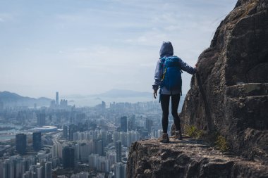 Kadın gezgin Hong Kong manzarasını görmek için uçurumun kenarına tırmanıyor.