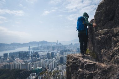 Kadın gezgin Hong Kong manzarasını görmek için uçurumun kenarına tırmanıyor.