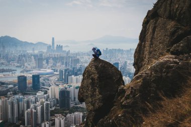 Uçurumun kenarında oturan kadın Hong Kong 'un güzel manzarasının tadını çıkar.