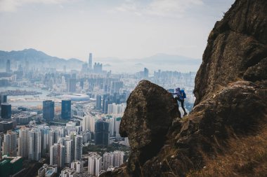 Kadın gezgin Hong Kong manzarasını görmek için uçurumun kenarına tırmanıyor.