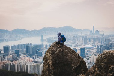 Uçurumun kenarında oturan kadın Hong Kong 'un güzel manzarasının tadını çıkar.
