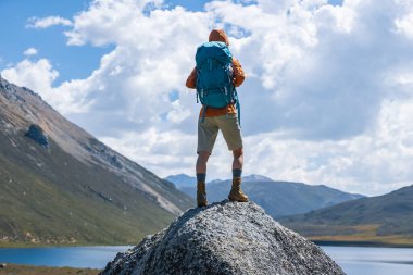Sırt çantalı bir kadın yüksek irtifada dağ tepesinde yürüyüş yapıyor. Uzakta bir göl var.