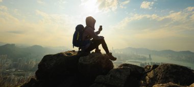 Başarılı kadın yürüyüşçü, Hong Kong 'da akıllı telefonuyla selfie çekerken uçurumun kenarında oturur.