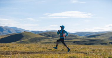 Yüksek irtifada koşan kadın izci otlağın tepesindeki yolda koşuyor.